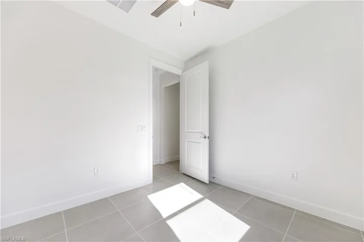 Room featuring light grey tile flooring, white baseboards, and a modern ceiling fan with a wood-finish