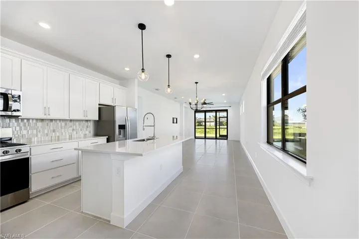Open-concept kitchen and living area featuring a large island with sink, white shaker cabinetry, stainless steel appliances, and a mosaic tile backsplash