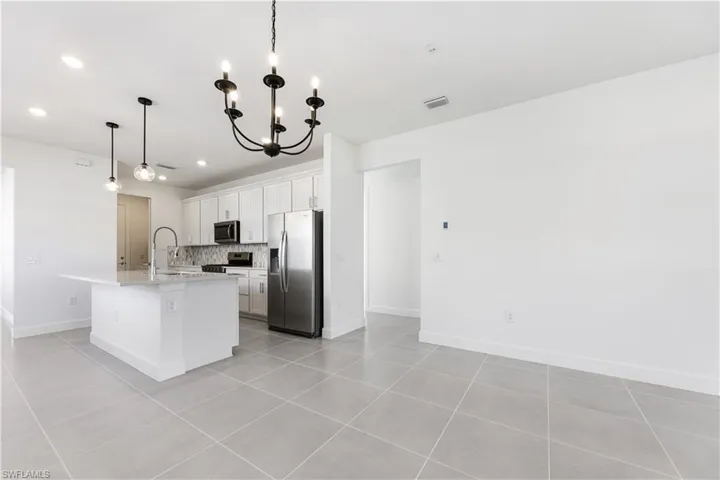 Bright kitchen featuring white shaker cabinetry, stainless steel appliances, a center island with pendant lighting, and a mosaic tile backsplash