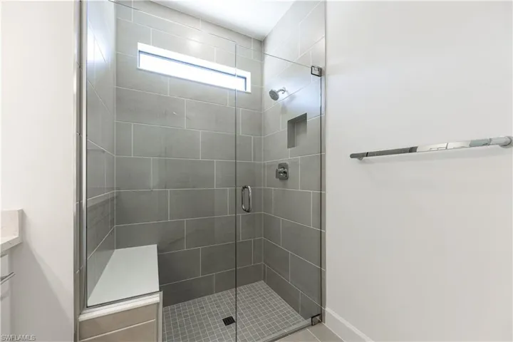 Glass-enclosed shower featuring large format gray tile, a built-in bench, and an integrated shower niche