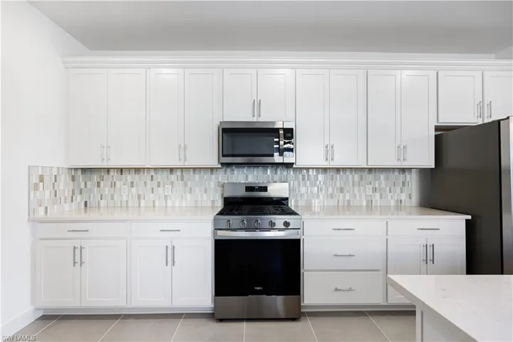 Kitchen featuring white shaker cabinetry, stainless steel range and microwave, light countertop, and mosaic tile backsplash