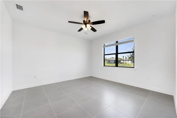Spacious room featuring large format tile flooring, a window with roller shade, white baseboards, and a ceiling fan with integrated lighting