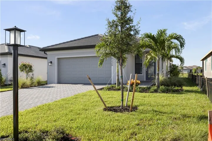 Contemporary stucco exterior featuring a two-car garage, concrete tile roof, paver driveway, and established palm trees