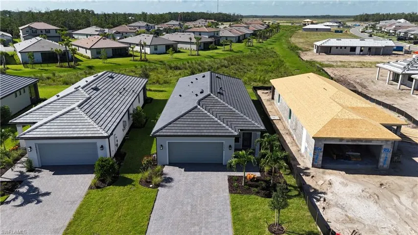 Contemporary residential facade featuring a light gray exterior, dark gray tile roof, two-car garage, paver driveway, and manicured landscaping