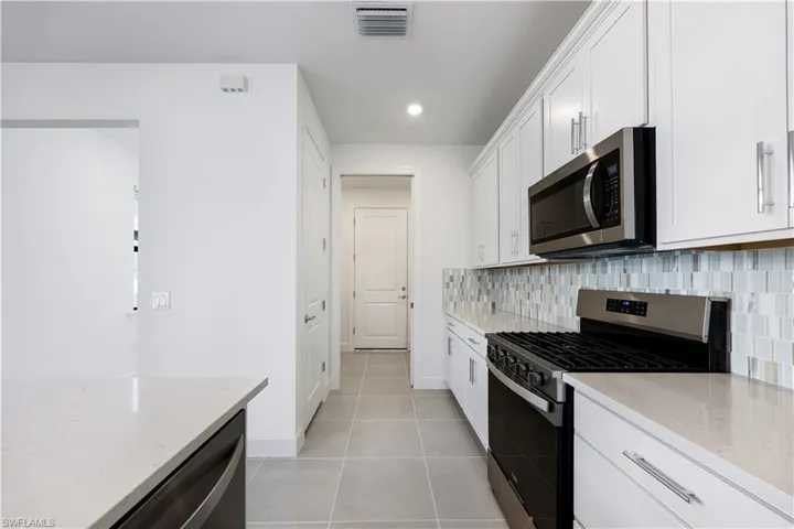 Modern kitchen featuring white shaker cabinetry, stainless steel appliances including a built-in microwave and gas range, light-toned countertops, and a mosaic tile backsplash