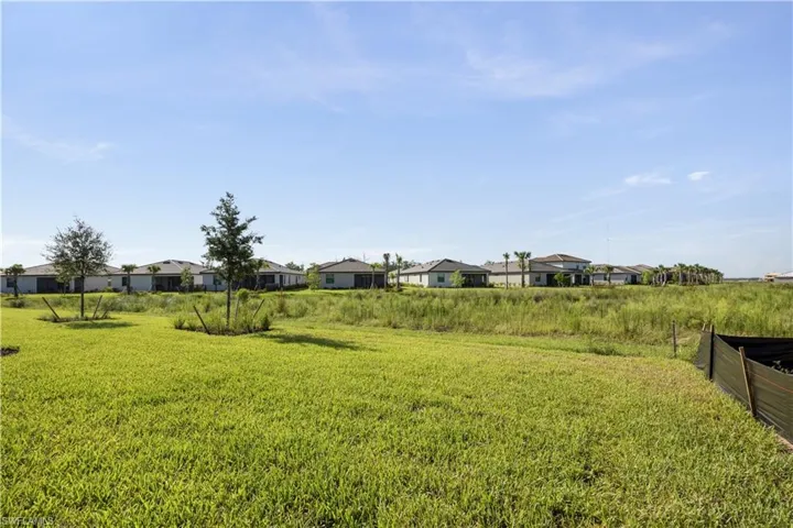Expansive undeveloped land featuring natural vegetation and a distant row of residential structures