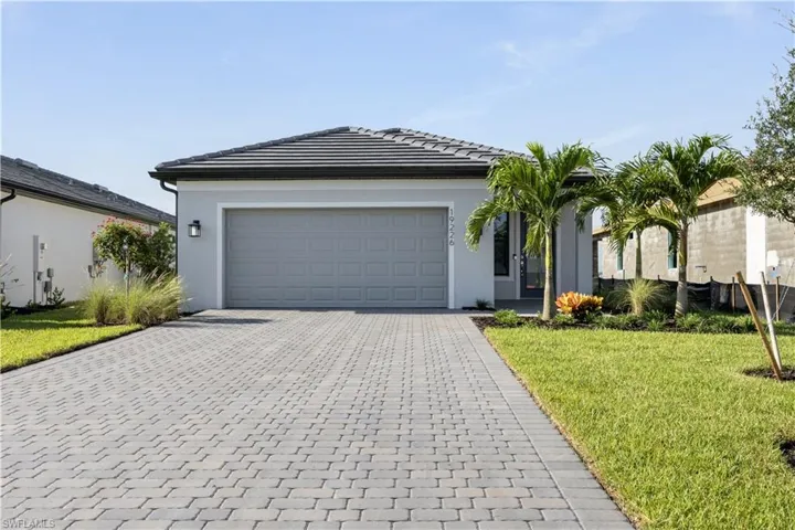 Modern single-story home featuring a paver driveway, an attached garage, and a tile roof