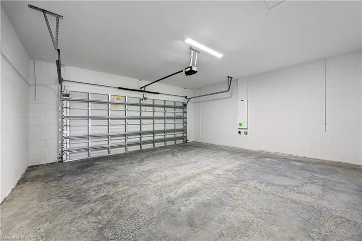 Spacious garage featuring a concrete floor, painted concrete block walls, overhead garage door opener, and fluorescent lighting