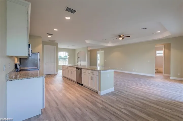 Kitchen with light stone counters, a kitchen island with sink, a raised ceiling, and recessed lighting