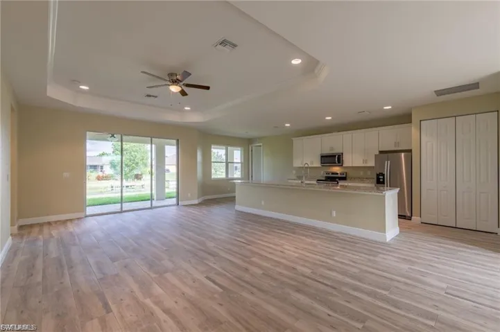 Kitchen with a tray ceiling, a center island with sink, open floor plan, light wood-type flooring, and recessed lighting