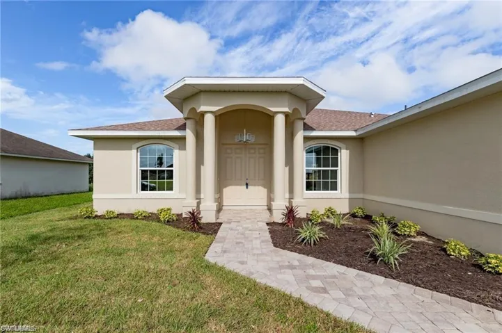 Property entrance featuring stucco siding, a lawn, and a shingled roof