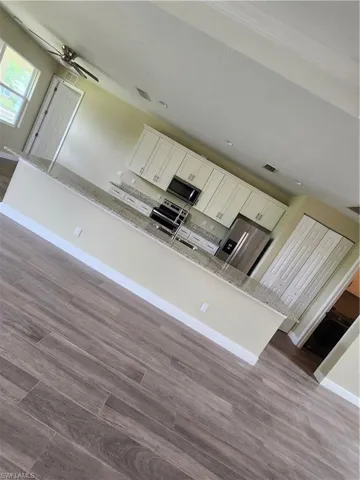 Kitchen featuring white cabinets, dark wood-type flooring, light stone countertops, and stainless steel microwave