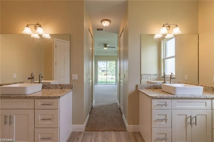 Bathroom with a chandelier, two vanities, light wood-style floors, and a ceiling fan