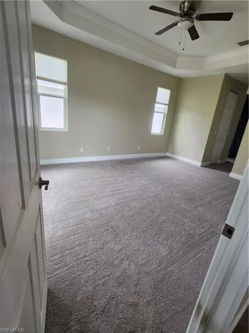 Spare room featuring a raised ceiling, carpet, crown molding, and a ceiling fan