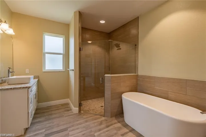 Full bath featuring a soaking tub, vanity, light wood finished floors, a shower stall, and tile walls