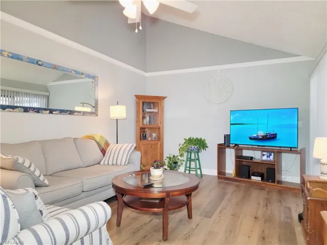 Living room with high vaulted ceiling, ornamental molding, a ceiling fan, wood finished floors, and baseboards