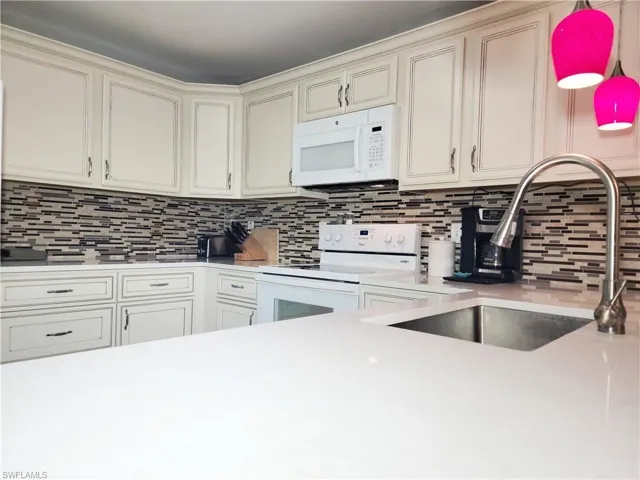 Kitchen with white appliances, light countertops, tasteful backsplash, and a sink