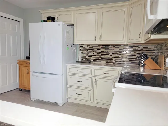 Kitchen featuring ventilation hood, freestanding refrigerator, light countertops, cream cabinetry, and tasteful backsplash