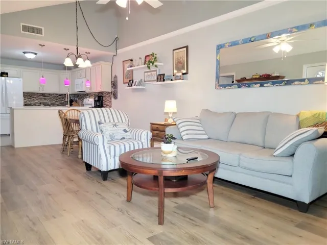 Living area with visible vents, ceiling fan with notable chandelier, light wood-style floors, and vaulted ceiling