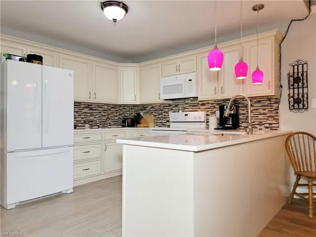 Kitchen with white appliances, a peninsula, a sink, decorative backsplash, and light countertops