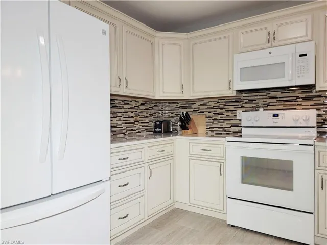 Kitchen featuring cream cabinetry, white appliances, light countertops, and decorative backsplash