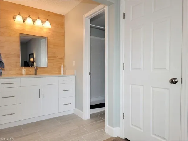 Bathroom with vanity, wooden walls, baseboards, and a textured ceiling
