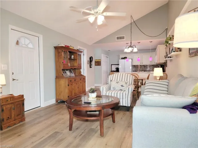 Living room featuring visible vents, light wood finished floors, baseboards, and ceiling fan with notable chandelier