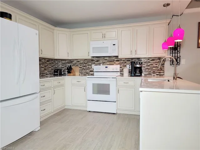 Kitchen featuring decorative backsplash, white appliances, light countertops, and a sink