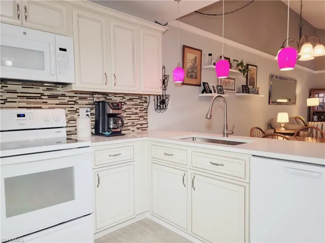 Kitchen with light countertops, decorative backsplash, hanging light fixtures, white appliances, and a sink