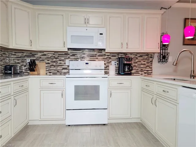 Kitchen featuring decorative backsplash, white appliances, light countertops, and a sink