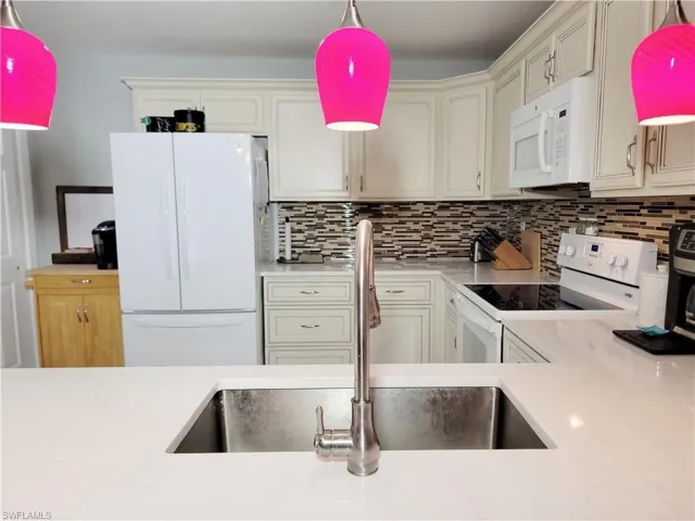 Kitchen with white appliances, a sink, hanging light fixtures, light countertops, and backsplash