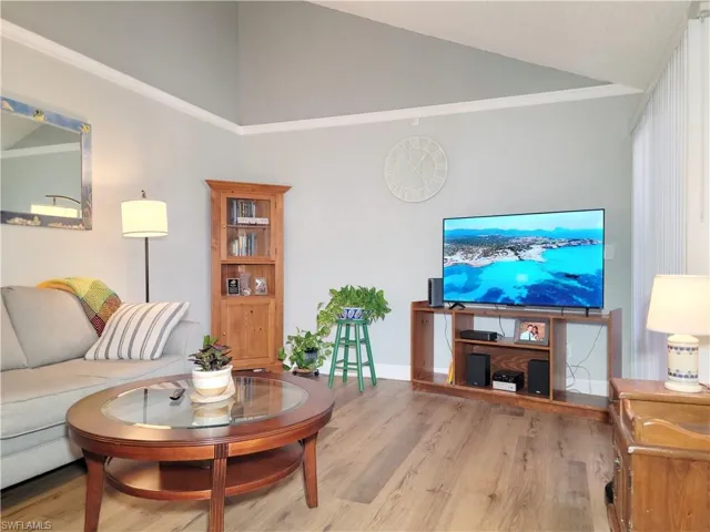 Living room with vaulted ceiling, crown molding, wood finished floors, and baseboards