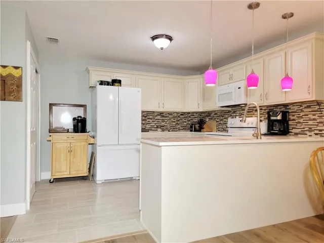 Kitchen featuring visible vents, light countertops, decorative backsplash, a peninsula, and white appliances