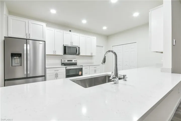 Kitchen featuring white cabinets, appliances with stainless steel finishes, a peninsula, light stone counters, and recessed lighting