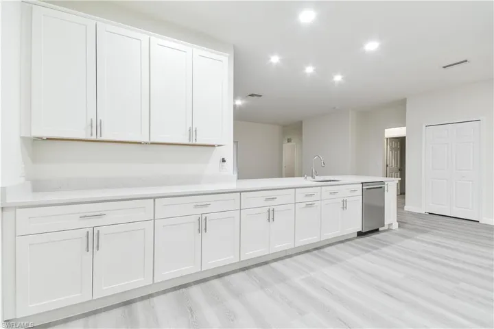 Kitchen featuring white cabinets, light wood finished floors, a peninsula, stainless steel dishwasher, and light stone countertops