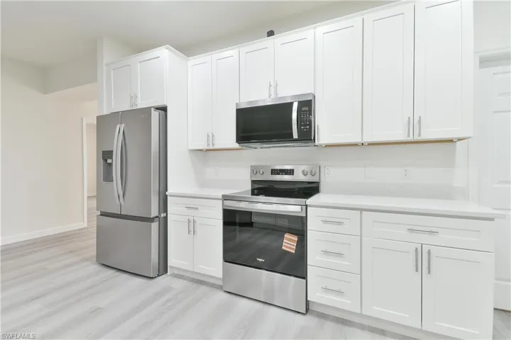 Kitchen featuring stainless steel appliances, white cabinetry, light wood-style flooring, and light stone counters