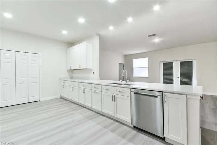Kitchen with stainless steel dishwasher, white cabinets, a peninsula, light wood finished floors, and light stone counters