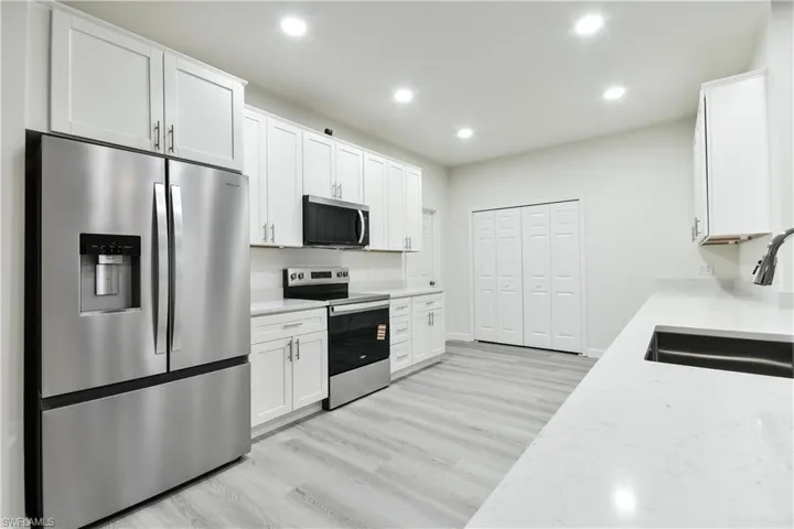 Kitchen with appliances with stainless steel finishes, light wood finished floors, recessed lighting, white cabinetry, and light stone countertops