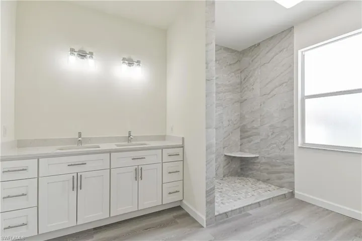 Bathroom featuring double vanity, light wood finished floors, and a walk in shower