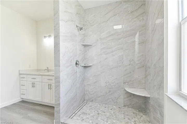 Full bathroom with vanity, tiled shower, and light wood-style floors
