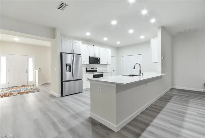 Kitchen with appliances with stainless steel finishes, white cabinetry, a peninsula, light wood-style flooring, and recessed lighting
