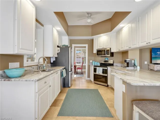 Kitchen with white cabinets, stainless steel appliances, light stone countertops, a tray ceiling, and a peninsula