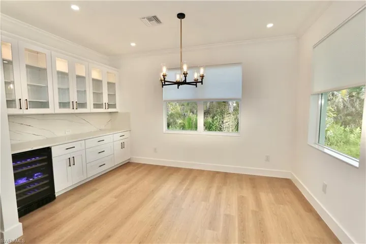 Dry Bar featuring glass insert cabinets, hanging light fixtures, healthy amount of natural light, beverage cooler, and ornamental molding