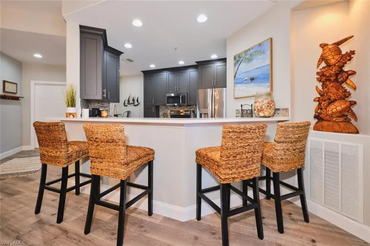 Kitchen with a breakfast bar area, stainless steel appliances, backsplash, light wood-type flooring, and gray cabinetry