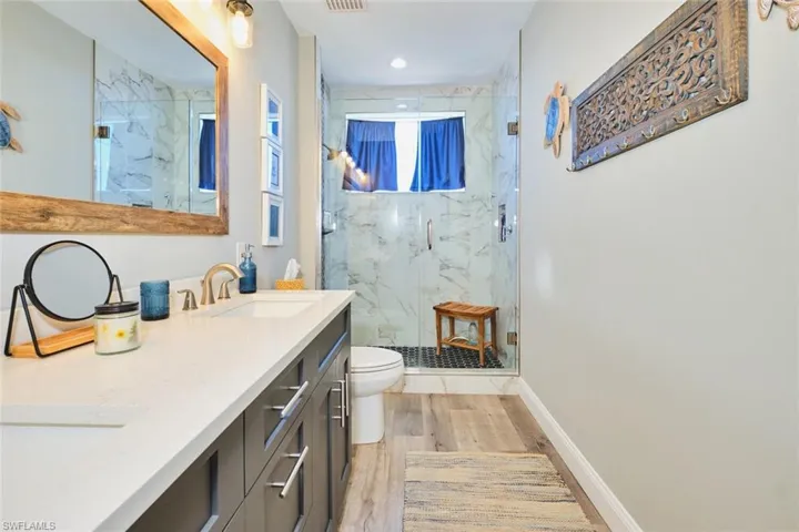 Bathroom featuring double vanity, a marble finish shower, and light wood-type flooring