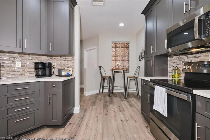 Kitchen featuring stainless steel appliances, backsplash, light wood-style flooring, light stone countertops, and gray cabinets