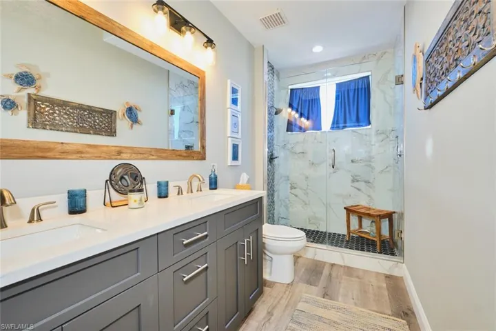 Bathroom featuring double vanity, a marble finish shower, and light wood-type flooring