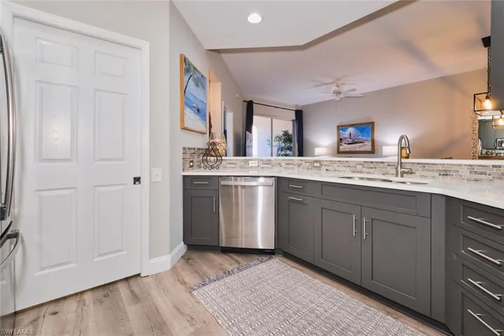Kitchen with stainless steel appliances, ceiling fan, gray cabinetry, backsplash, and light stone counters