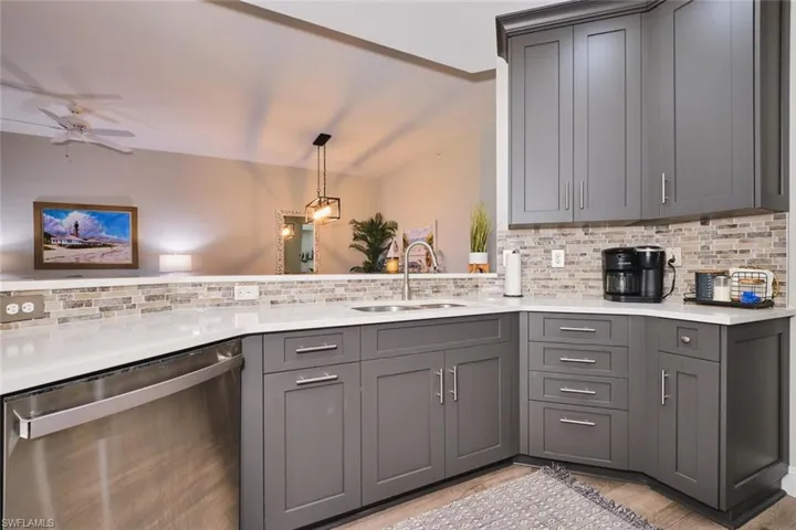 Kitchen featuring dishwasher, gray cabinetry, decorative backsplash, and light stone counters