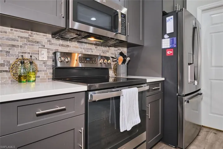 Kitchen featuring stainless steel appliances, gray cabinetry, decorative backsplash, light stone counters, and light wood-style floors